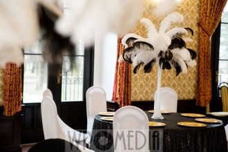 Dekoracja sali weselnej z czarnym obrusem z połyskiem, białymi krzesłami i piórami Czarno-biała dekoracja w sali weselnej