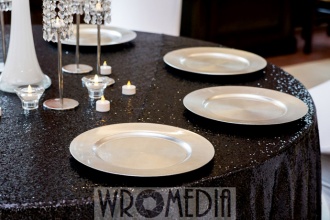 Stół weselny z czarnym cekinowym obrusem i srebrnymi podtalerzami Stół weselny z czarnym cekinowym obrusem i srebrnymi podtalerzami